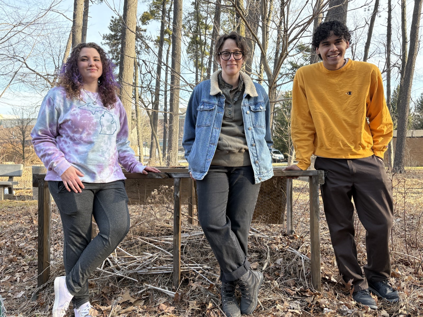 Three people leaning up against the compost in the WCC Food Forest