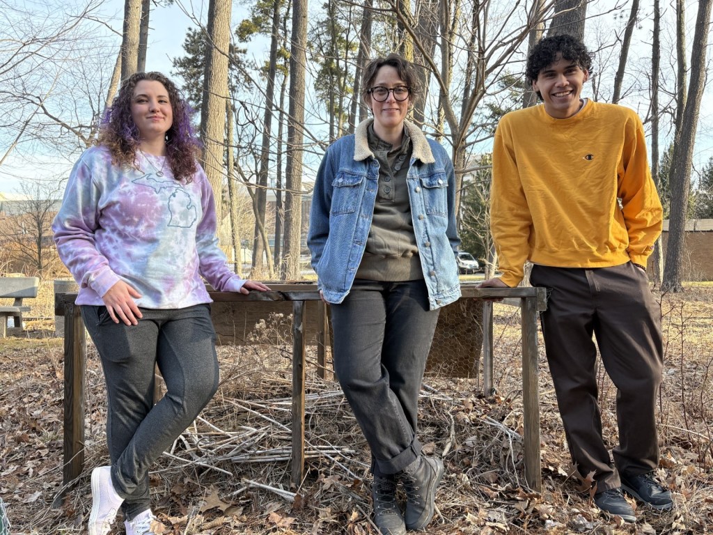 Three people leaning up against the compost in the WCC Food Forest